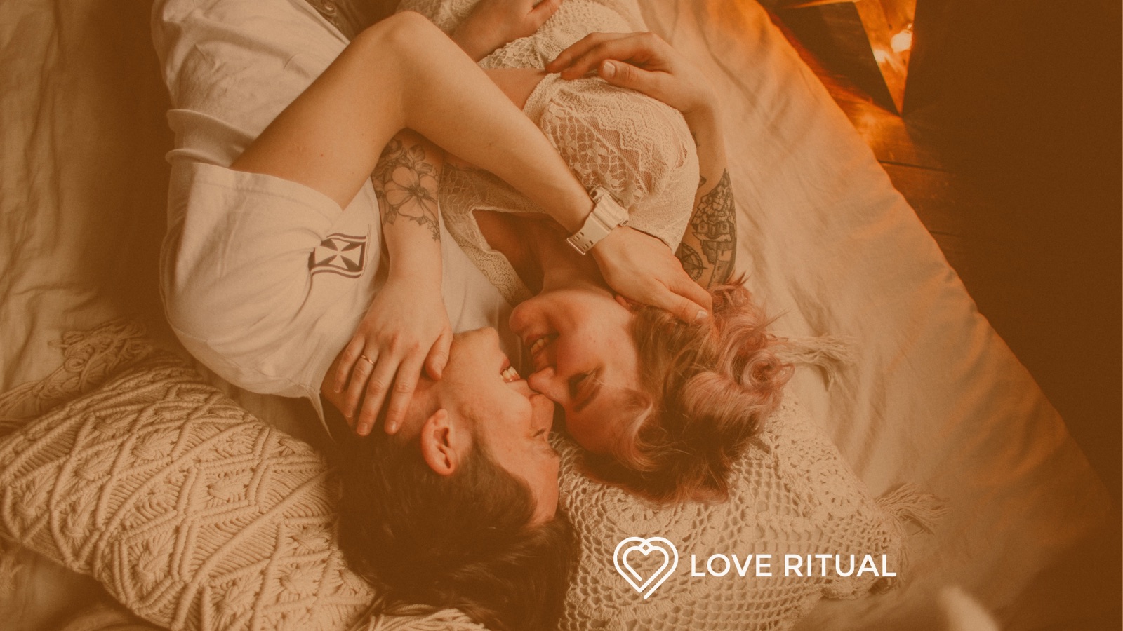 A couple lying on a bed facing each other and smiling, seen from above