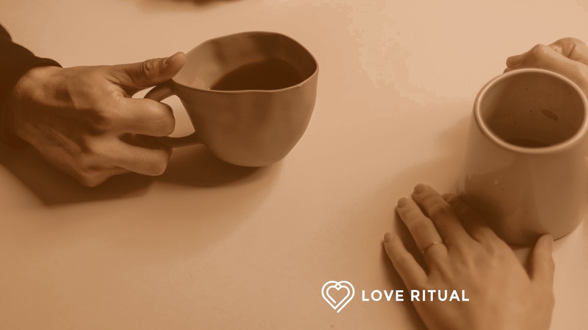 Two people sitting across from each other at a table, each holding a cup of coffee