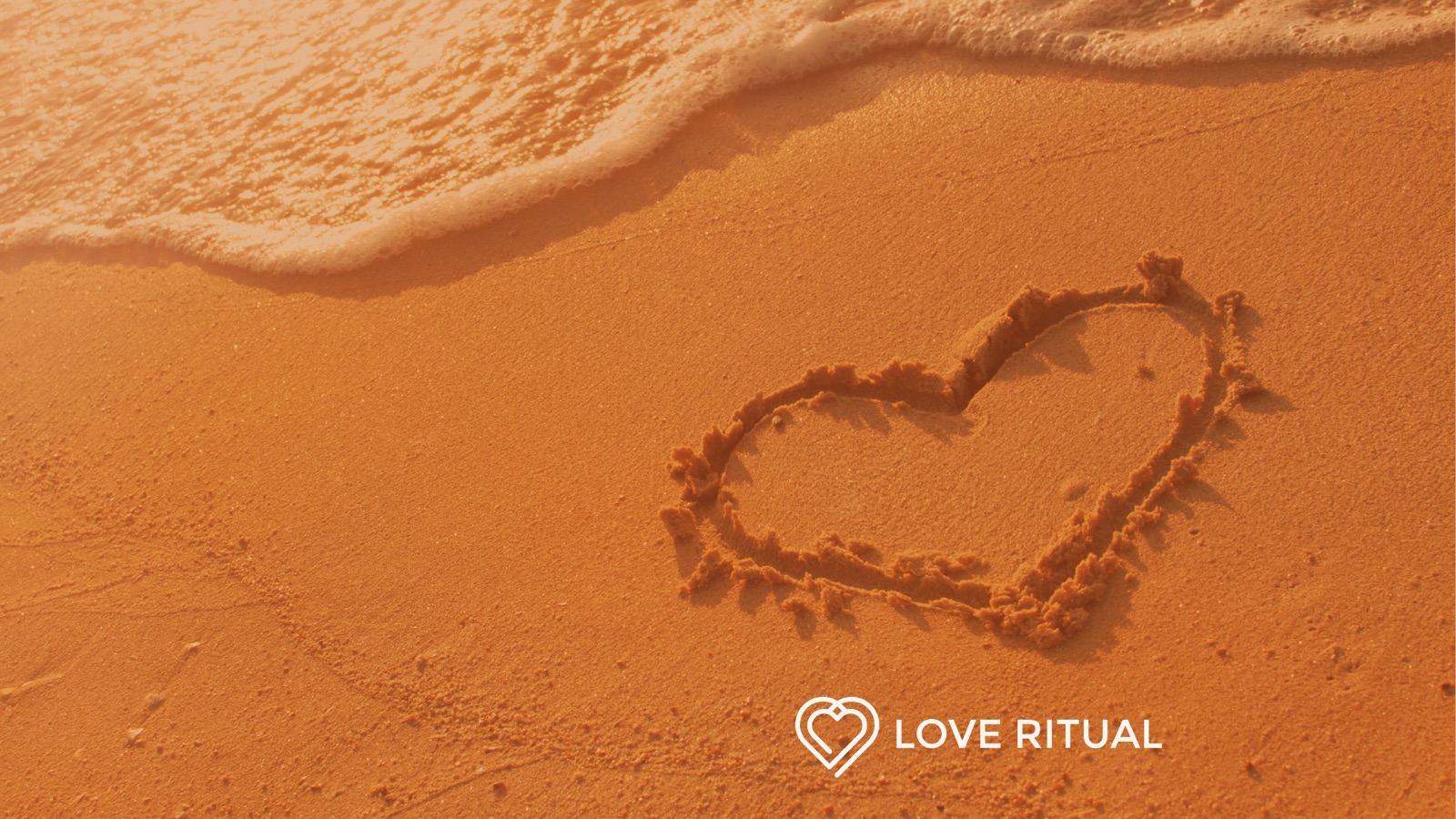 A heart drawn in wet sand as a wave washes up the beach